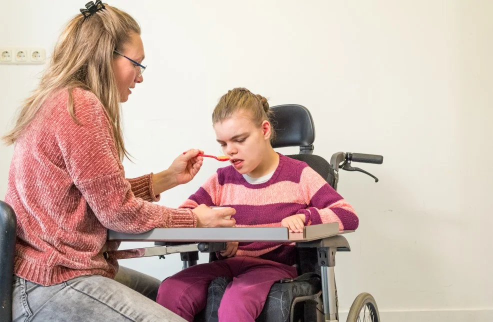 Disabled girl in wheelchair being fed by support worker