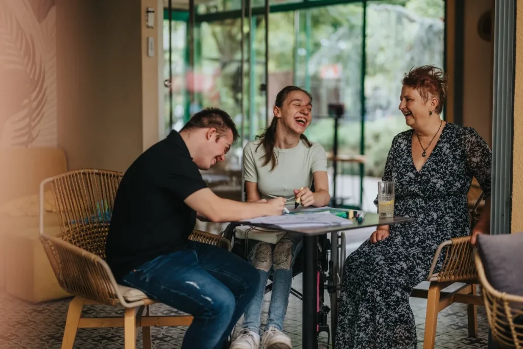Two disabled friends drawing and laughing with support worker