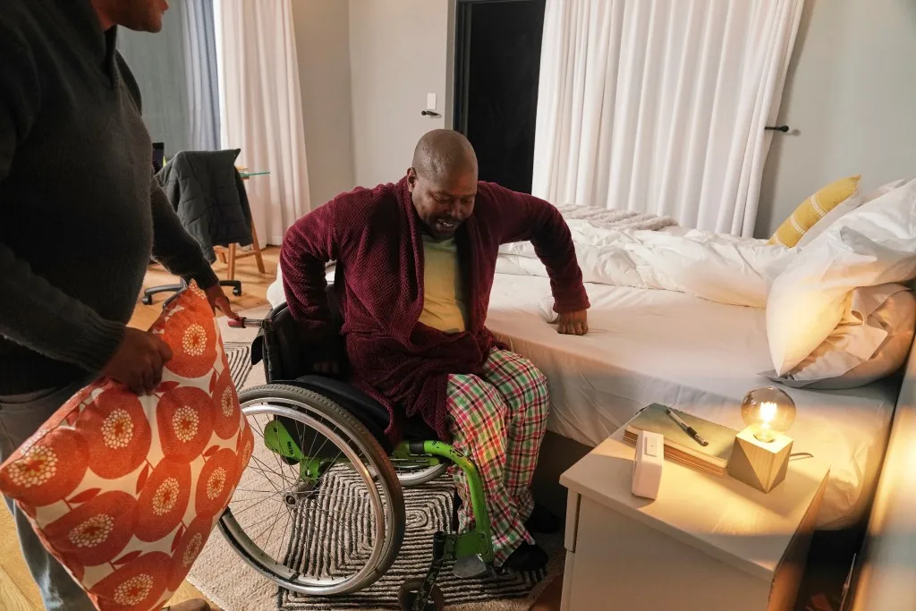 Disabled man in wheelchair getting into bed with help of support worker