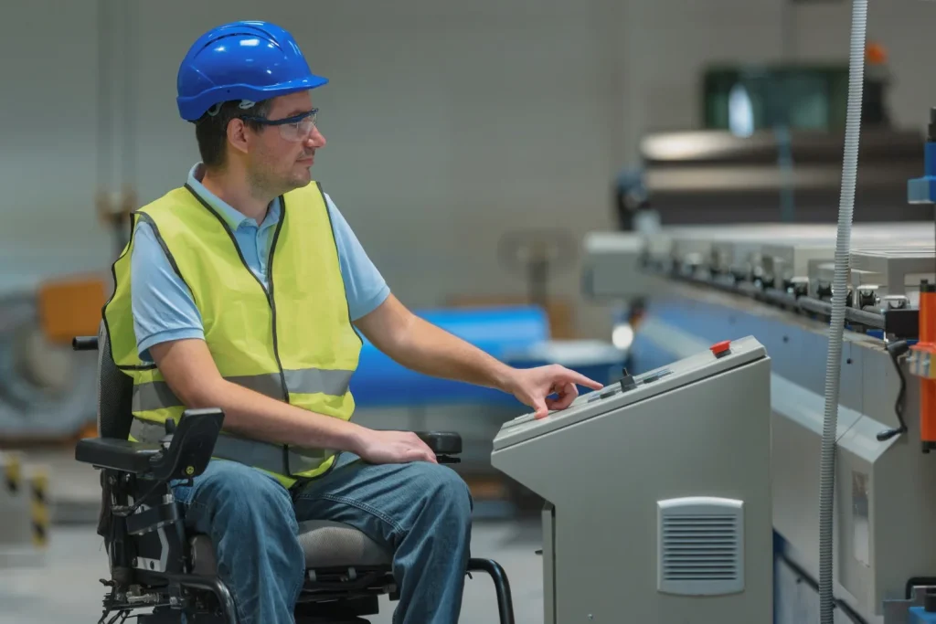 Disabled man in wheelchair wearing hard hat and hi vis vest, operating machinery at work