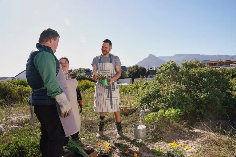 Two disabled friends outside gardening with support worker